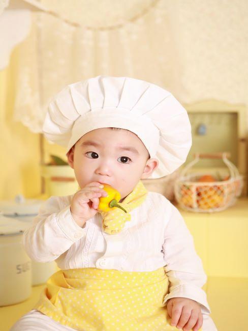 repas pour enfant petit garcon habille en chapeau blanc de chef en tablier jaune train de manger du poivron jaune