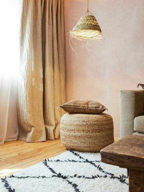 Wnętrze w stylu boho z jutowym pufem, poduszką, biało - czarnym dywanem oraz lampą