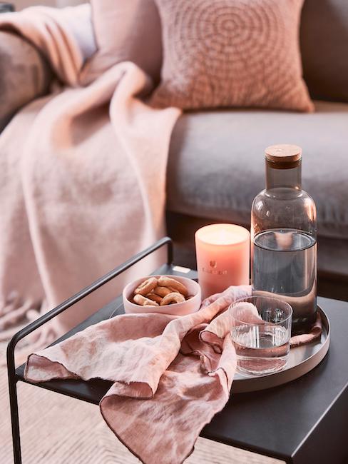 Couchtisch mit pastellrosa Leinen-Serviette auf Dekotablett vor Couch mit pastellrosanen Kissen und Decke