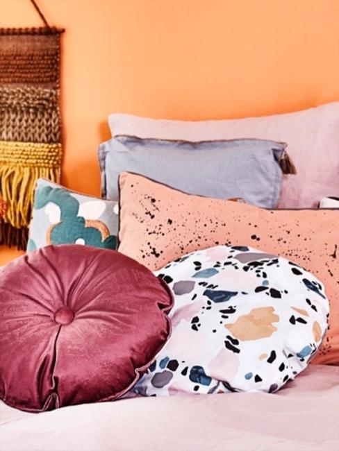 Coussins à motif terrazzo Coussin à imprimé terrazzo clair sur le lit devant le mur orange