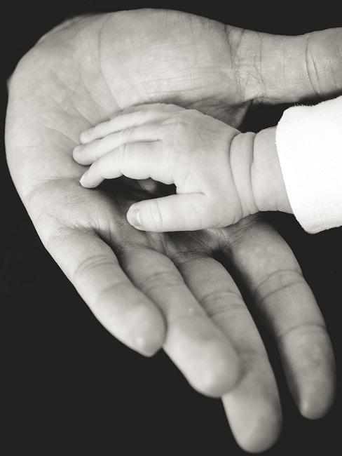 Babyhand auf Hand von Erwachsenem in Schwarz-Weiß