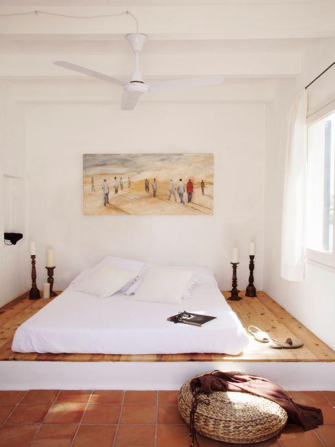 nettoyer un matelas chambre a coucher avec un matelas pose par terre, sur un podium en bois, dans une chambre aux murs blancs, tableau sur le mur et bougeoirs des deux cotes du lit