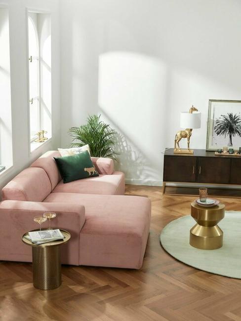 Jasny salon z różową, sztruksową sofą, stolikiem kawowym oraz komodą z drewna