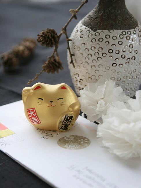 Złoty kot Maneki Neko na białym stoliczku, obok wazonu
