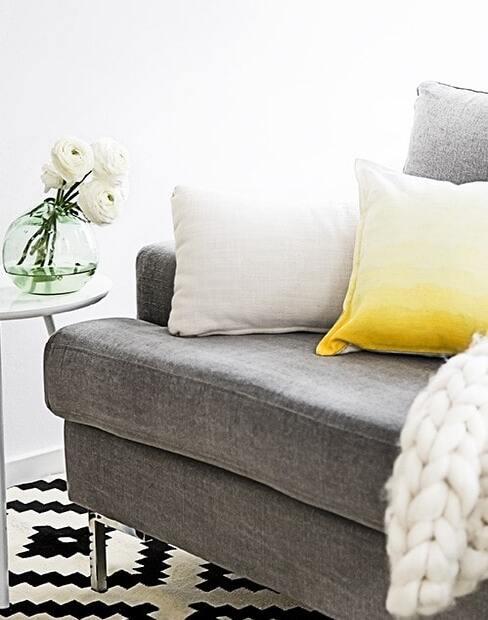 Szara sofa z biała poduszką oraz żółta poduszką we wzór ombre na biało - czarnym dywanie