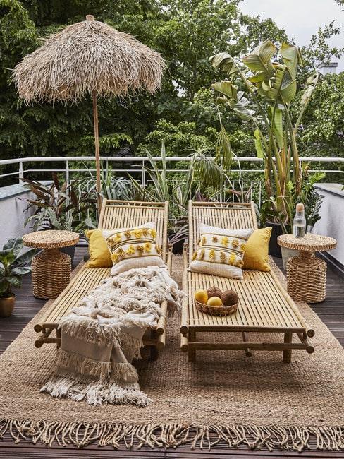 Balkon z dwoma leżakami z bambusa, parasol oraz jutowy dywan zewnętrzny z roślinami