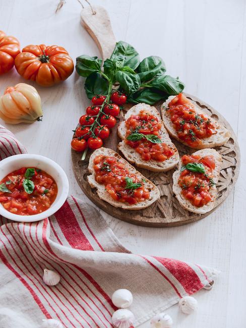 bruschetta na drewnianej desce do krojenia na białym blacie obok czerwonej ściereczki