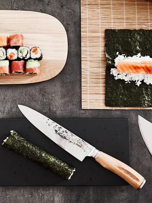 sushi robione w domu na czarnym blacie z nożem oraz maki na drewnianej desce