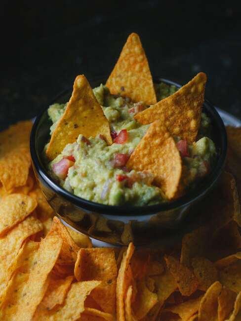 Domowe nachosy na białym talerzu z czarną miseczką guacamole