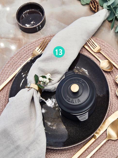 Gedekte tafel met borden, bestek en een linnen servet met gouden servetring
