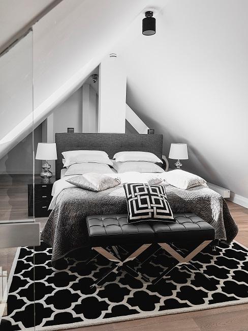 Schlafzimmer modern Schlafzimmer unter dem Dach mit Schräge in Schwarz-Weiß mit modernem grafischen Muster auf dem Teppich und einem Dekokissen