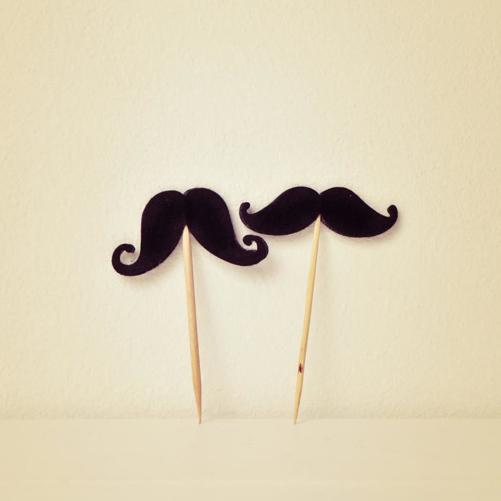 two different felt mustaches in sticks over a beige background, with a retro effect