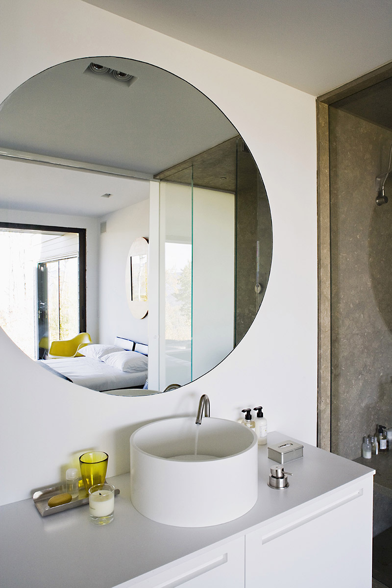 A white designer wash stand with bathing utensils and a round wall mirror
