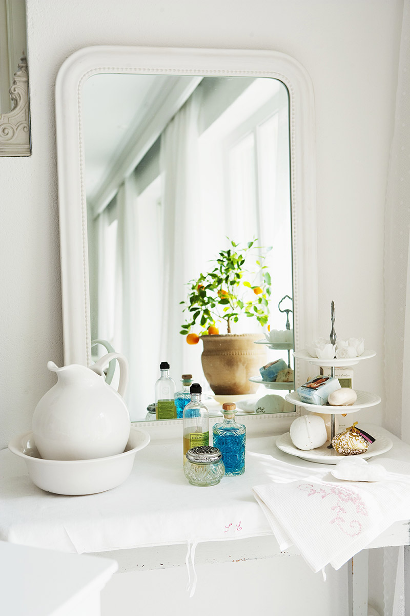 Mirror, washbasin and jug and soaps on cake stand in bathroom